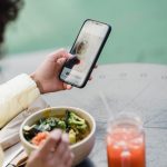 crop blogger with smartphone and tasty vegetarian salad in cafeteria